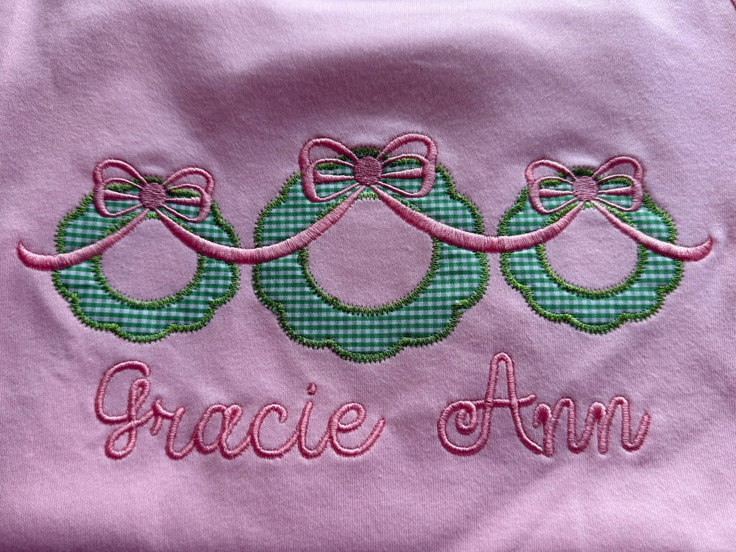 Embroidered design with green checkered bows and pink text on a light pink background