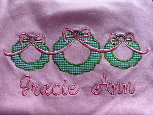 Embroidered design with green checkered bows and pink text on a light pink background