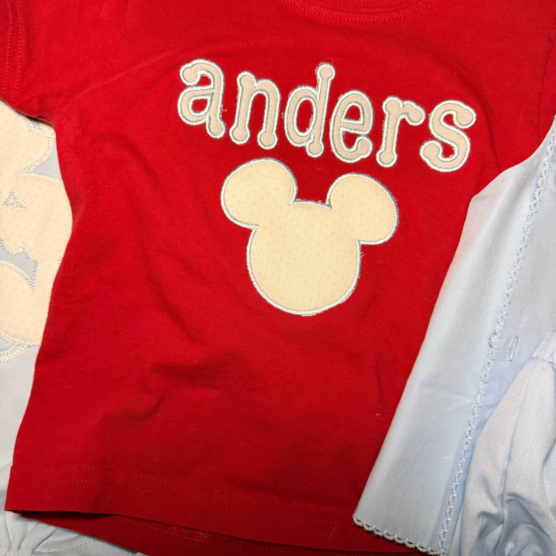 Red baby onesie with 'anders' and a Mickey Mouse head design on a light-colored surface.